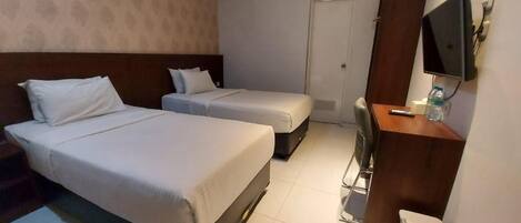 A hotel room with two beds, a desk, a chair, a television, and a trash bin.