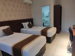 A hotel room with two beds, a desk, and a wardrobe. - Doho Homestay (Jember)