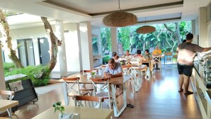 A spacious indoor dining area with wooden tables and chairs, large windows offering a view of lush greenery outside. - Doho Homestay (Jember)