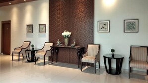 A lobby with a reception desk, two chairs, a small table, and decorative wall panels. - Doho Homestay (Jember)