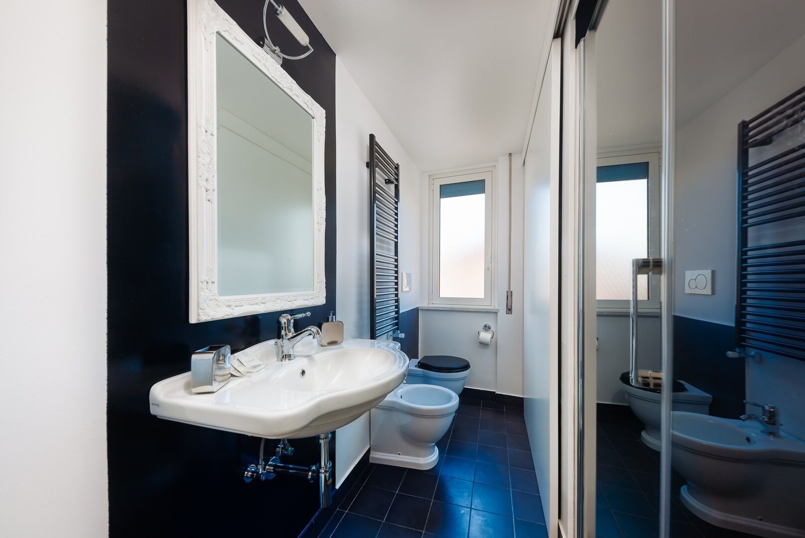 Un baño moderno con un espejo grande, un lavamanos blanco, un inodoro y un bidé.