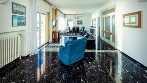 A spacious hallway with a black marble floor, a blue armchair, a dining area with a table and chairs, and artwork on the walls. - CASAVIVA - PRIMAVERA 1a RAPALLO (Zoagli)