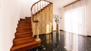 A wooden staircase with a curved design, leading to a landing area with a decorative panel and a vase with branches. - CASAVIVA - PRIMAVERA 1a RAPALLO (Zoagli)