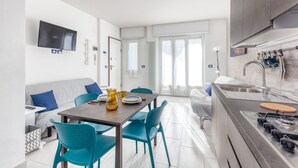A modern kitchen with a dining area, a TV mounted on the wall, and a large window with curtains. - Casaviva - Val Del Ponte 5 Sanremo (Sanremo)