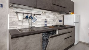 A modern kitchen with grey cabinets, a stainless steel sink, a built-in dishwasher, a gas stove, and a white refrigerator. - Casaviva - Val Del Ponte 5 Sanremo (Sanremo)