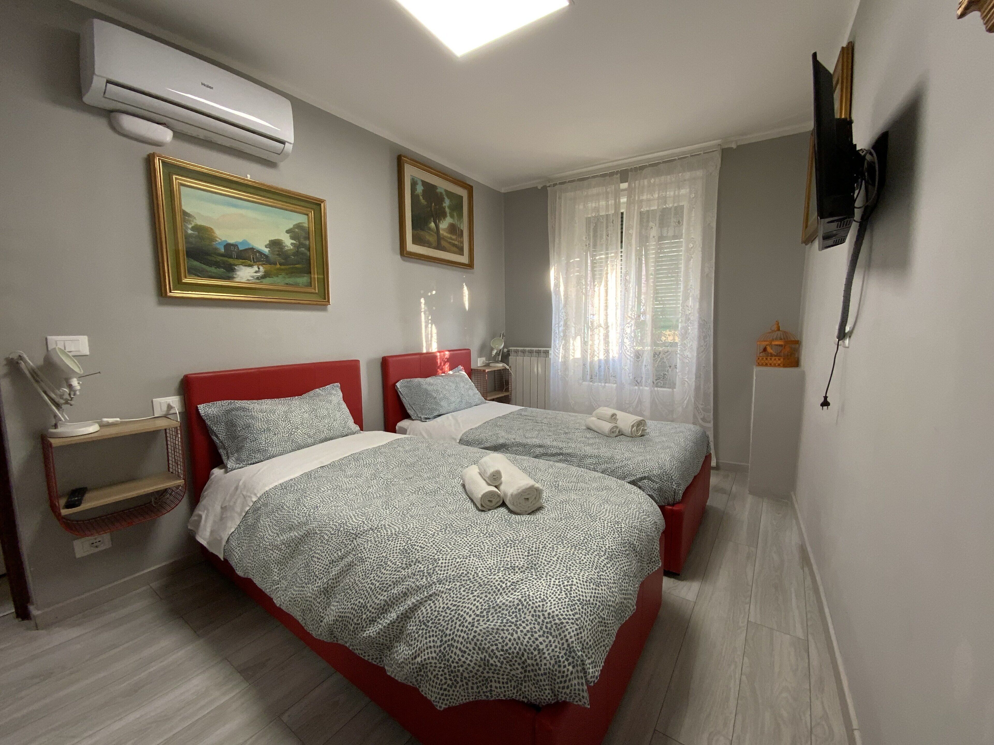 A hotel room with two beds, a desk, a chair, an air conditioner, and a TV mounted on the wall.