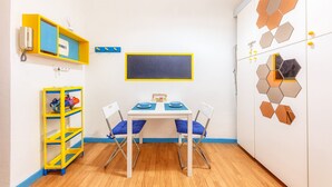 A child's playroom with a table, chairs, a chalkboard, and a wardrobe with geometric wall art.