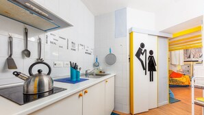 A modern kitchen with white cabinets, a kettle, and utensils hanging on the wall. There's a sink and a blue mat on the counter.