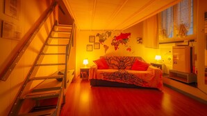 A bedroom with a bed, a ladder, a desk, a lamp, a map on the wall, and a refrigerator.