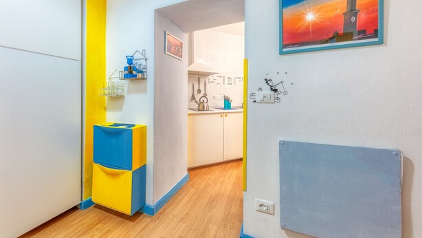 A modern kitchen with white cabinets, a yellow and blue cabinet, and a painting of a lighthouse.
