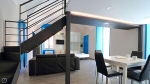 Moderni hotellihuone, jossa on portaikko, sohva, ruokapöytä tuoleineen ja sänky.