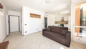 Una sala de estar moderna con un sofá, una puerta que da a una cocina y un ventanal a un espacio exterior.