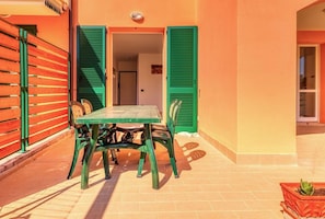 An outdoor patio with a table and chairs, green shutters, and a potted plant.