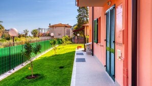 Un edificio con un balcón, un césped verde y una cancha de tenis al fondo.