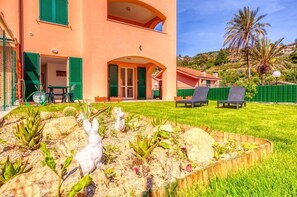 A two-story building with a garden in the foreground, featuring a white rabbit sculpture, green plants, and a wooden fence. - CasaViva - Pasteur 277 Bordighera (Bordighera)