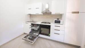Una cocina moderna con armarios blancos, lavavajillas integrado, microondas y campana extractora de acero inoxidable.