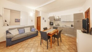 A compact living space with a sofa, dining table, chairs, a kitchen area, and a television. - CasaViva - Mameli 26 Imperia (Imperia)