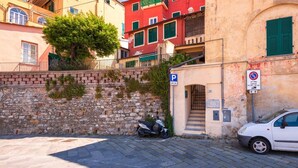 A narrow cobblestone street with a parked scooter and a white car, a stone wall, and colorful buildings with green shutters. - CasaViva - Mameli 26 Imperia (Imperia)