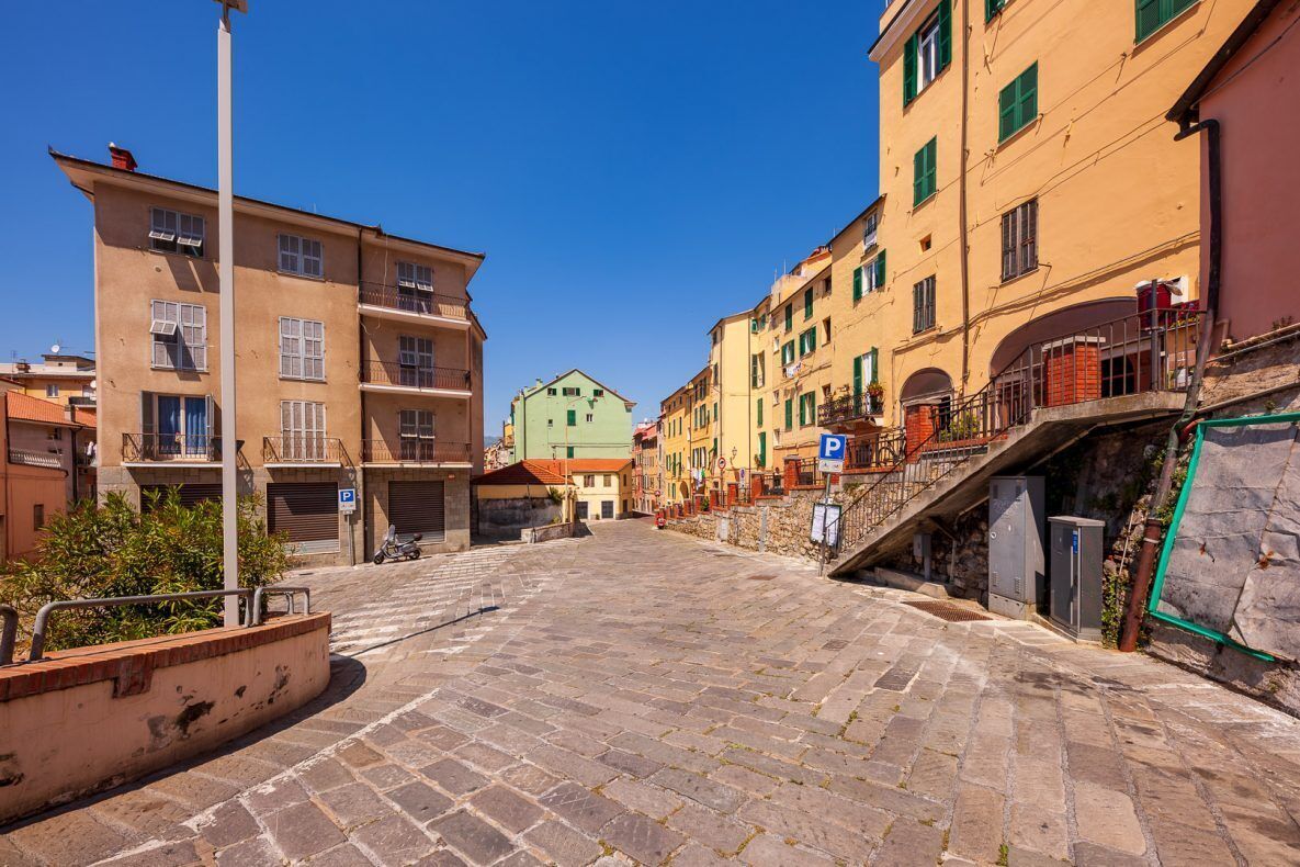 Une rue pavée bordée de bâtiments des deux côtés, un ciel bleu dégagé et un panneau de signalisation indiquant un espace de stationnement.