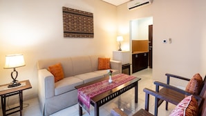 A living room with a sofa, a coffee table, and a lamp. There is a patterned wall hanging above the sofa. - Samawa Transit Hotel (Sumbawa Besar)