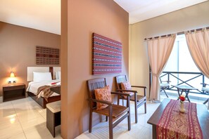 A hotel room with a bed, two wooden chairs, a small table with a vase, a nightstand, and a window with curtains. - Samawa Transit Hotel (Sumbawa Besar)