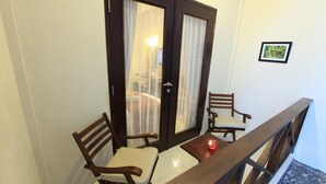 A balcony with a wooden table and two chairs, a door with curtains, and a framed picture on the wall. - Samawa Transit Hotel (Sumbawa Besar)