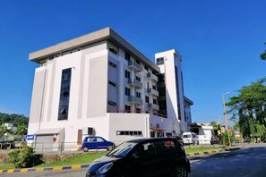 A multi-story building with a flat facade, several windows, and a parking area with cars. - Hotel Meligai Kapit (Kapit)