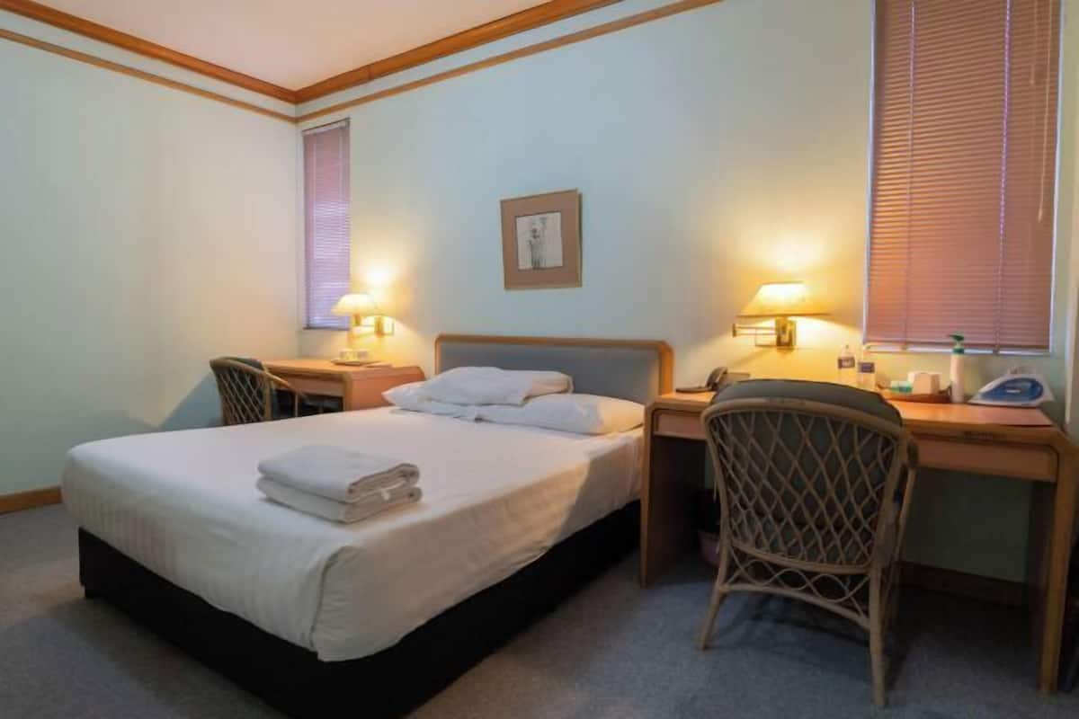 Hotellihuone, jossa on sänky, kaksi yöpöytää valaisimineen, työpöytä ja tuoli.