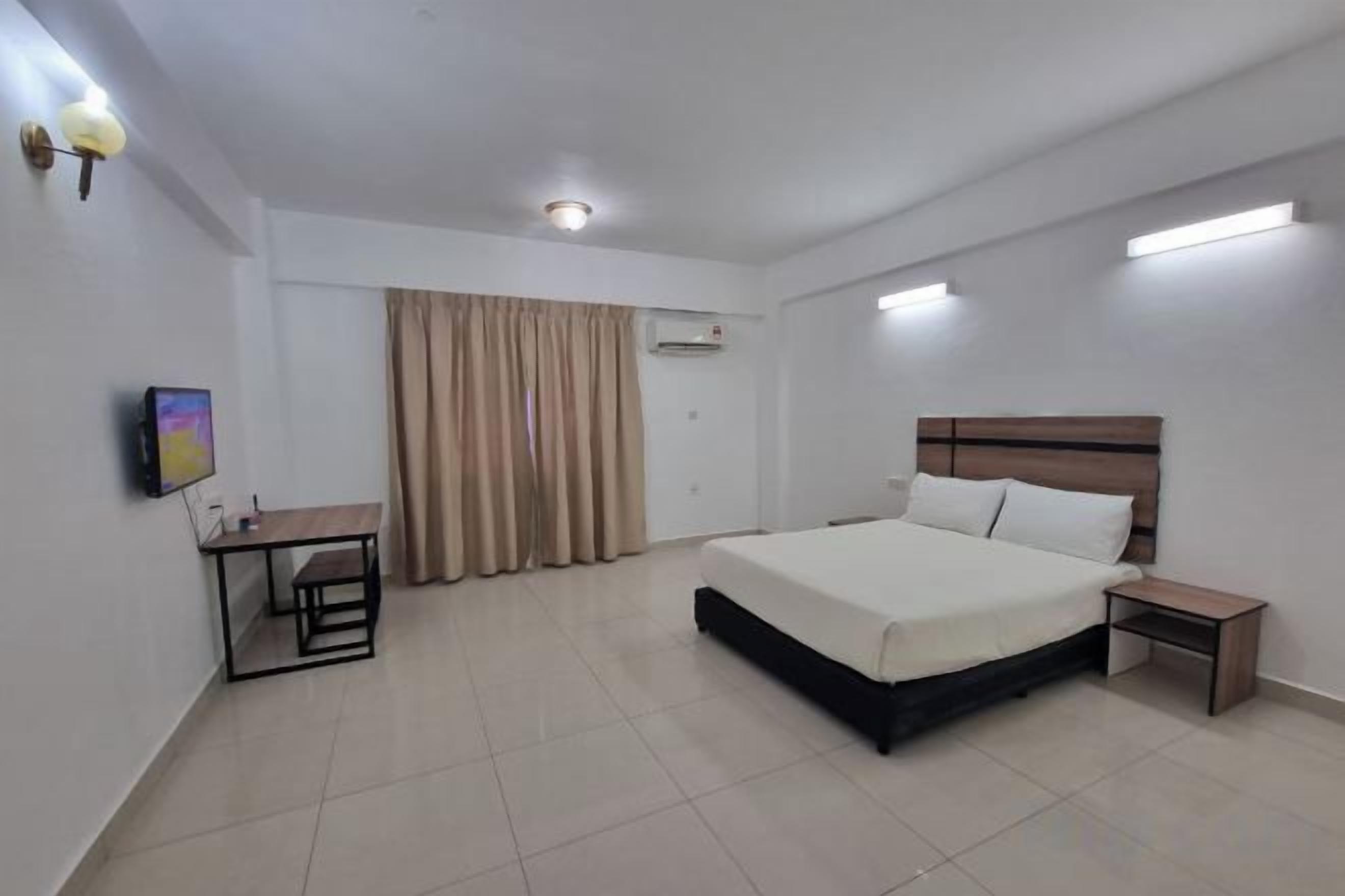 A hotel room with a bed, bedside table, desk, and curtains.
