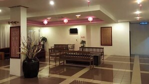 A lobby with a checkered floor, wooden benches, a large vase with dried plants, and a television on the wall.