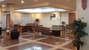 A spacious lobby with a high ceiling, recessed lighting, and a large skylight. There are several wooden benches and a potted plant.