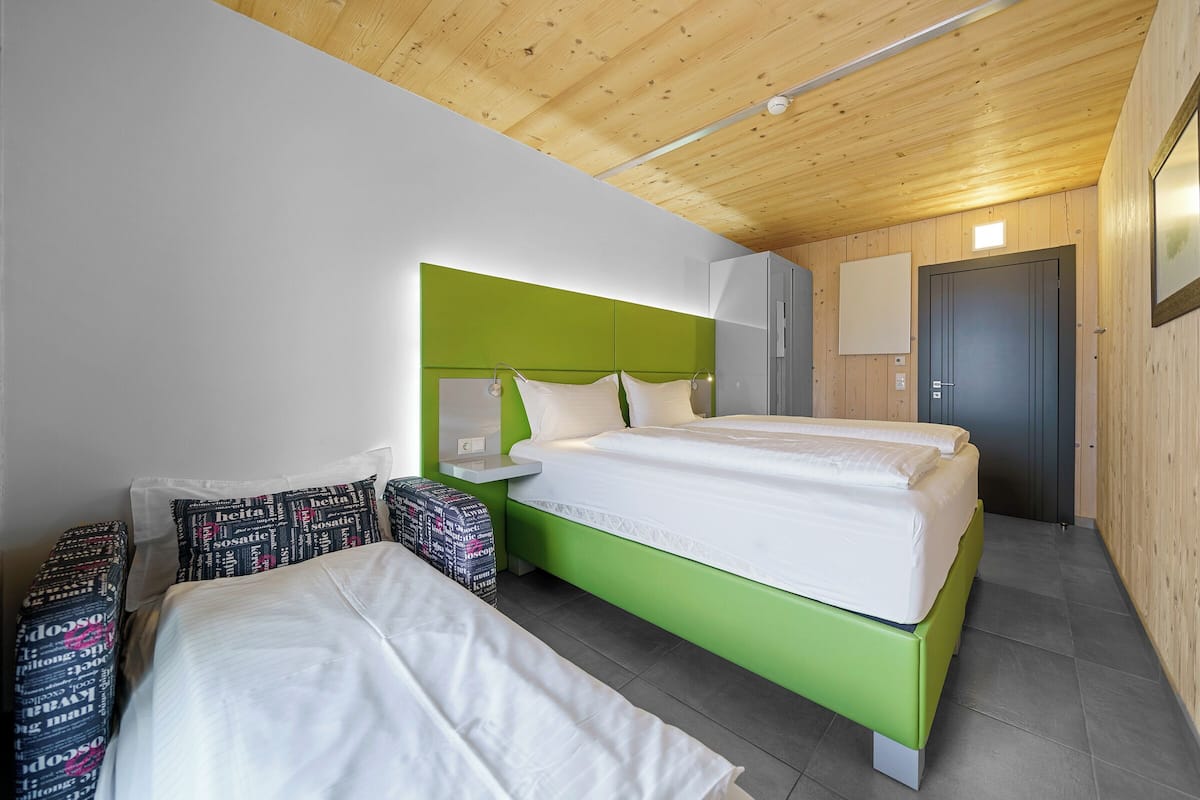 A room with a bed, a bedside table, a mirror, a door, and a wall-mounted light fixture.