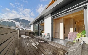 A wooden deck with a view of a mountain, a fan, and a wicker chair. - Aparthotel Zell am See (Zell am See)