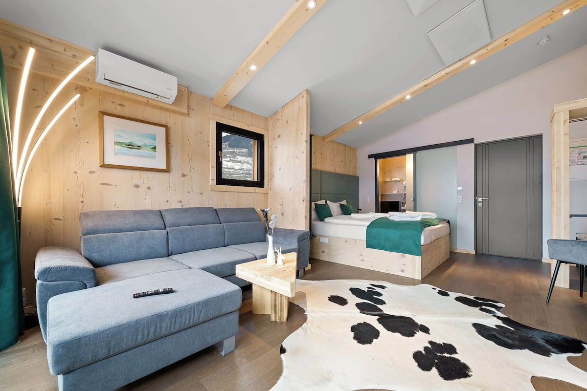 A modern interior with a sofa, a bed, a cowhide rug, and a wooden ceiling.