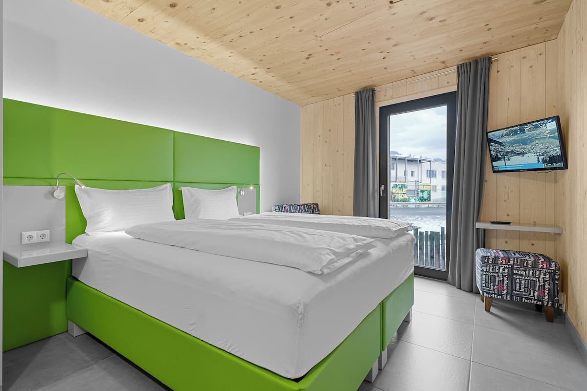 A modern hotel room with a green accent wall, a large bed, a television, and a view of the outside.
