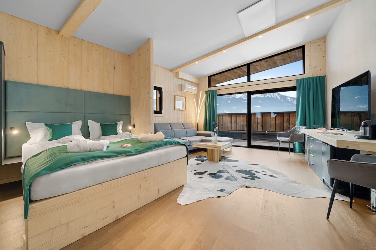 A modern hotel room with a large bed, a sofa, a desk, and a view of mountains.