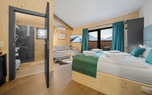 A modern hotel room with a bed, a sofa, a TV, and a view of mountains. - Aparthotel Zell am See (Zell am See)