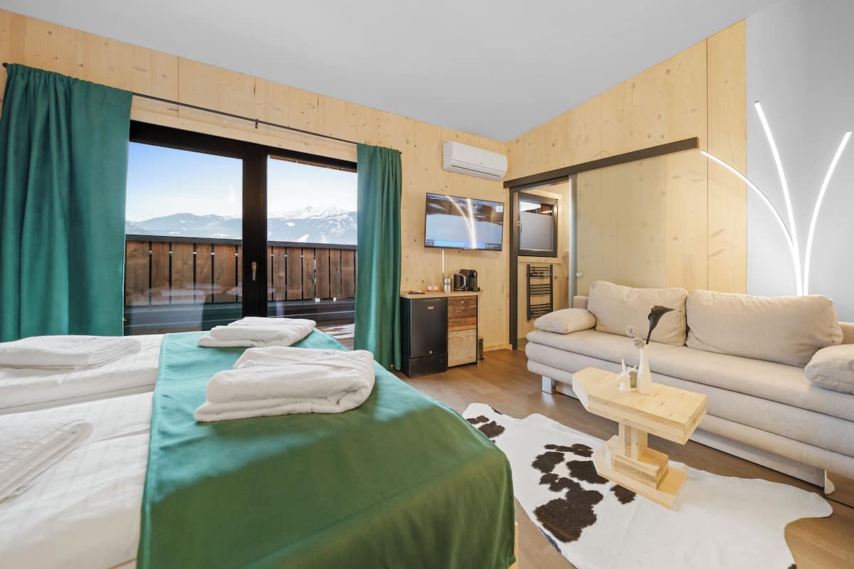 A hotel room with a bed, a sofa, a TV, a small desk, and a view of mountains.