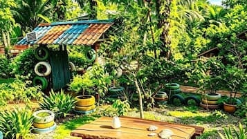 A garden with a wooden table, a small structure with a tin roof, and various potted plants.