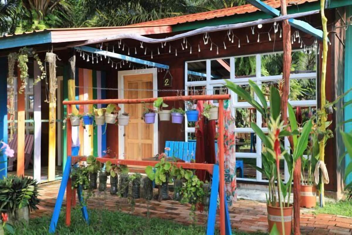 A colorful house with a wooden door, a small porch area, and a garden with potted plants and a swing set.