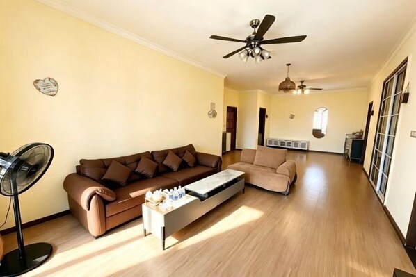 Un salon avec un canapé marron, une table basse, un ventilateur et un ventilateur de plafond.