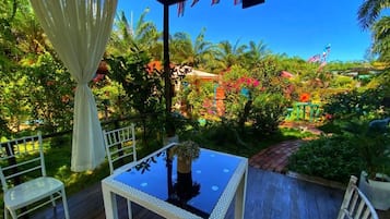 An outdoor patio with a table and chairs, surrounded by lush greenery and a clear blue sky.