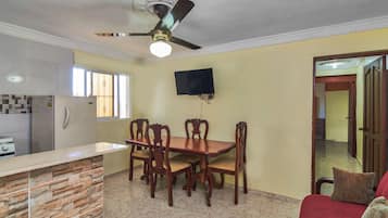 A dining area with a wooden table and chairs, a ceiling fan, and a TV mounted on the wall.