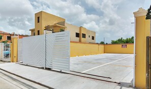 A gated parking area with a yellow building in the background. - Tropical Island Aparthotel (Santo Domingo Este)