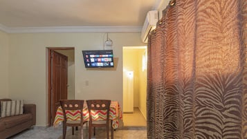 A living room with a sofa, a dining table with chairs, a flat-screen TV, and a patterned curtain.