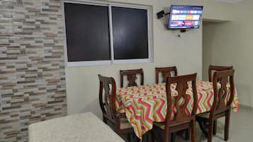 A dining area with a table set for four, a television mounted on the wall, and a stone-patterned wall.