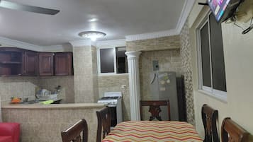 Una cocina con comedor, refrigerador, estufa y televisor montado en la pared.