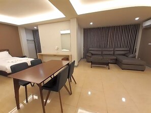 Une chambre d’hôtel comprenant un lit, une table à manger avec des chaises, un canapé, une petite table avec un miroir et une grande fenêtre avec des rideaux.