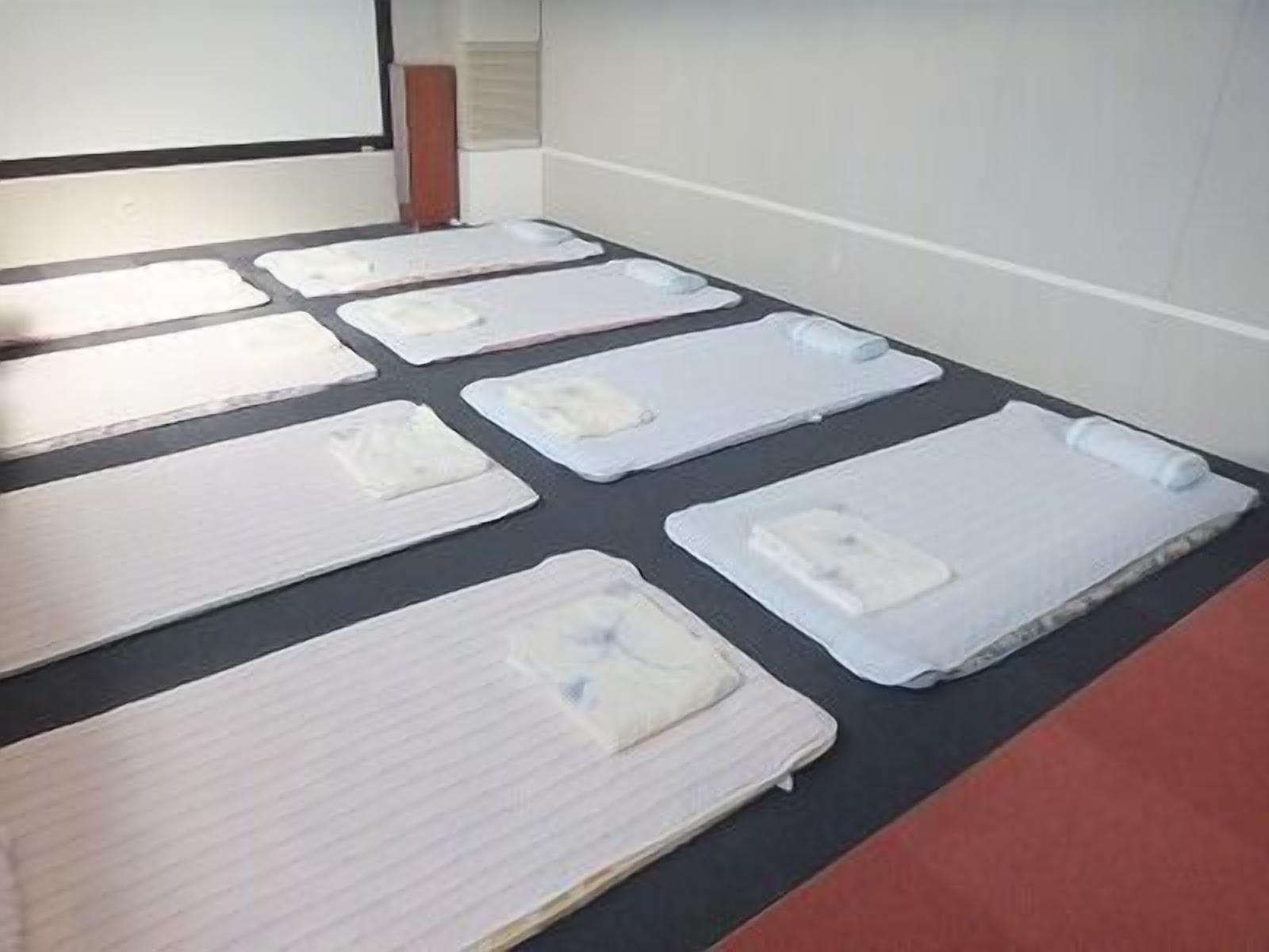 A room with multiple beds arranged in rows, each with a pillow and a blanket.