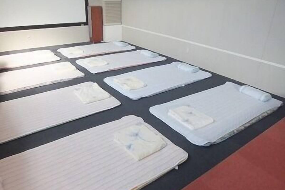 A room with multiple beds arranged in rows, each with a pillow and a blanket.